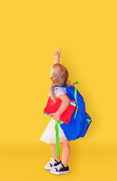 Little girl with pointing finger up at yellow background. Back to school. - Fotoğraf, Görsel