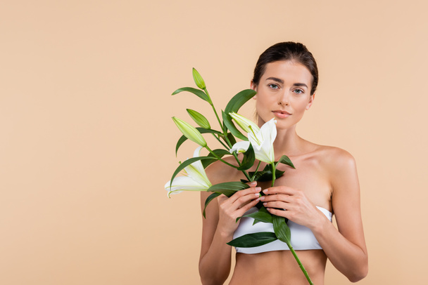 charming woman with white lily flowers looking at camera isolated on beige, beauty concept - Foto, Bild