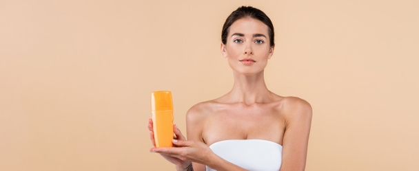 young woman in strapless top showing bottle of sunblock isolated on beige, banner - Foto, Imagem