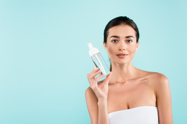 brunette woman in white strapless top showing face tonic isolated on blue - Φωτογραφία, εικόνα