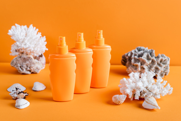 sea corals and bottles with sunscreen on orange background - Фото, изображение