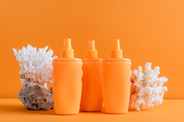 containers with sunblock near sea corals isolated on orange - Fotografie, Obrázek
