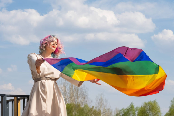 Caucasian woman with curly colored hair holding lgbt flag. Lesbian woman holding a rainbow flag outdoors - Фото, изображение