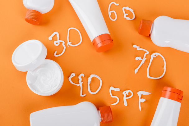 vista superior de protector solar y crema cosmética cerca de diferentes números y letras spf en naranja - Foto, imagen