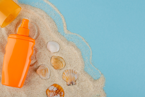 top view of orange sunblock bottle near seashells and sand on blue surface - Фото, изображение