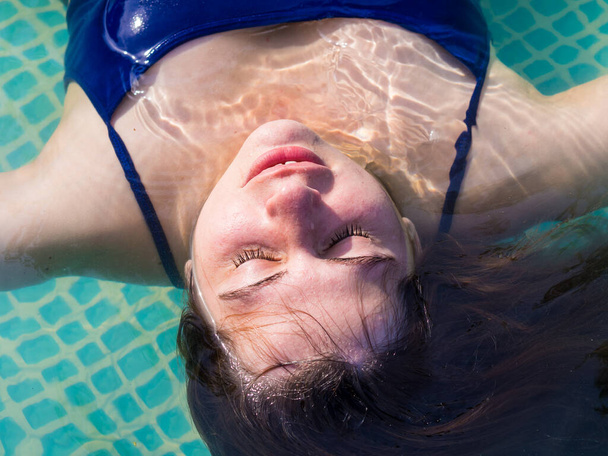 νεαρή κοπέλα σε μια ζεστή καλοκαιρινή μέρα χαλαρώνει στην πισίνα στο site της - Φωτογραφία, εικόνα