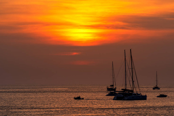 日没の背景と海のビーチでボートのシルエット。タイのプーケット島の海側での日没の瞬間 - 写真・画像