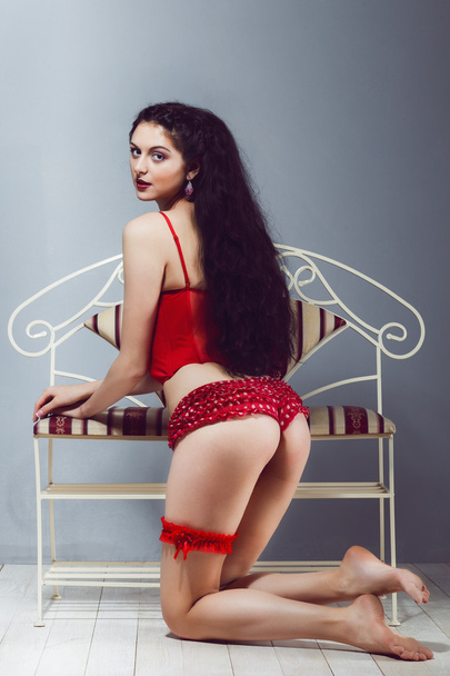 Sexy fille brune regarde en arrière tout en se tenant debout et tenant son cul en culotte rouge et talons corset avec jarretière dans le studio
 - Photo, image