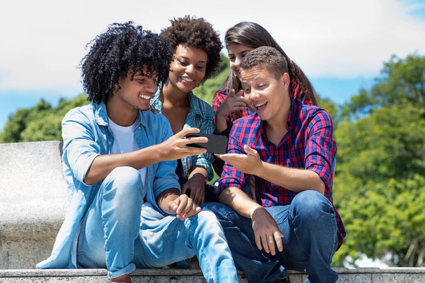 Hispanic influencer with mobile talking with other young adults outdoor in summer in city - Foto, imagen
