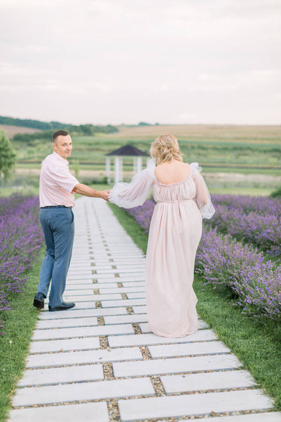 romantic mature couple in love walking on pathway through flowering lavender field - Foto, Imagen