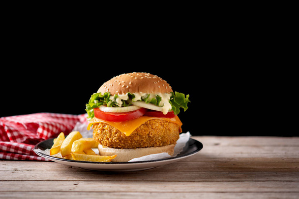 Crispy chicken burger with cheese and french fries on wooden table. Copy space - Photo, Image