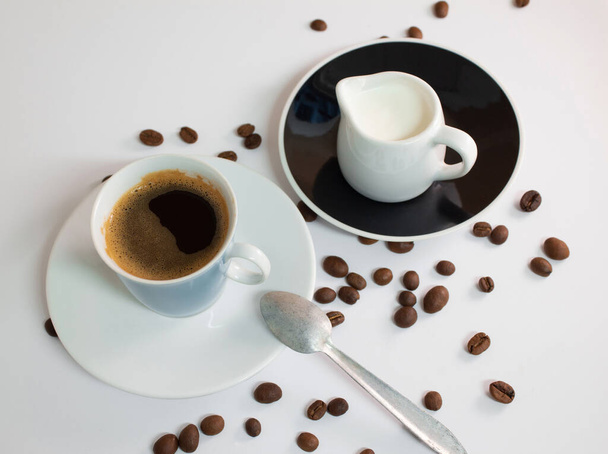 白いテーブルの上にクリームとコーヒー豆とコーヒー - 写真・画像