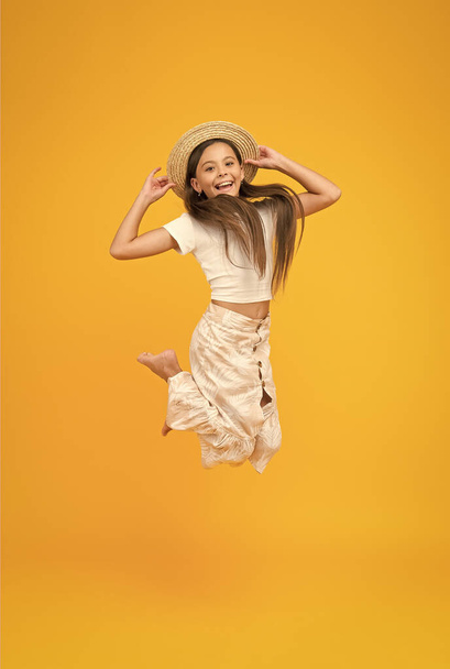 super active child jump in straw hat. barefoot kid feel freedom. full of happiness. summer kid fashion. little girl jumping high on yellow background. energetic kid on vacation - Photo, Image