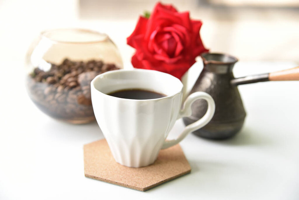 A cup of coffee, a turk, a red rose and coffee beans on a white table - Photo, Image