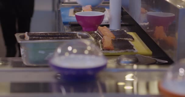 Köstliches Sushi auf dem Tisch neben Tellern am Fließband zubereiten - Filmmaterial, Video