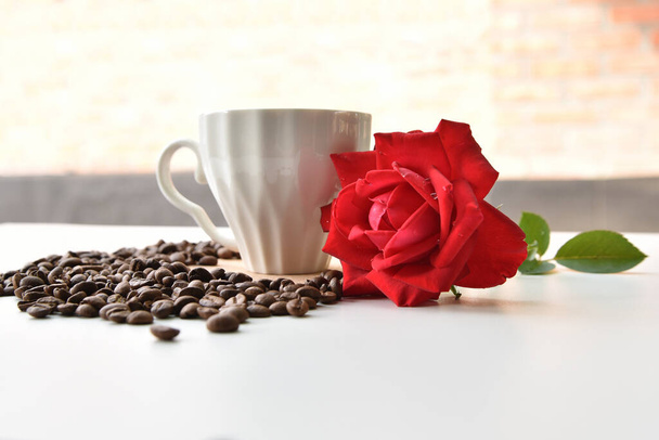 A rose, a cup and scattered roasted coffee beans - Foto, imagen