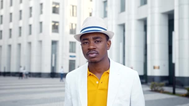 Zwarte man in pak met fedora hoed loopt langs straat glimlachend - Video