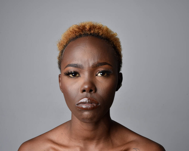 頭を閉じて、自然な髪を持つかなり若いアフリカの女性の肩の肖像画。感情的な表情をしています。明るい灰色のスタジオの背景に隔離されています. - 写真・画像