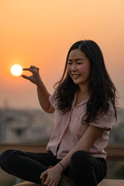 Ασιάτισσα Κινέζα Ταϊλανδέζα παίζει με το σχήμα του ήλιου στην ταράτσα σε ώρα λυκόφωτος. - Φωτογραφία, εικόνα