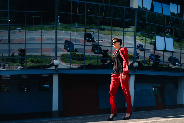 A girl in a red suit stands against the background of a modern building in the city. - 写真・画像