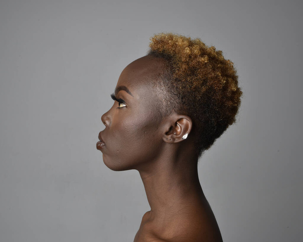 頭を閉じて、自然な髪を持つかなり若いアフリカの女性の肩の肖像画。感情的な表情をしています。明るい灰色のスタジオの背景に隔離されています. - 写真・画像