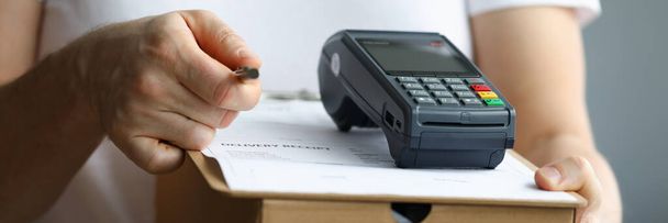 Courier holds cardboard box with payment terminal and documents with pen - Zdjęcie, obraz