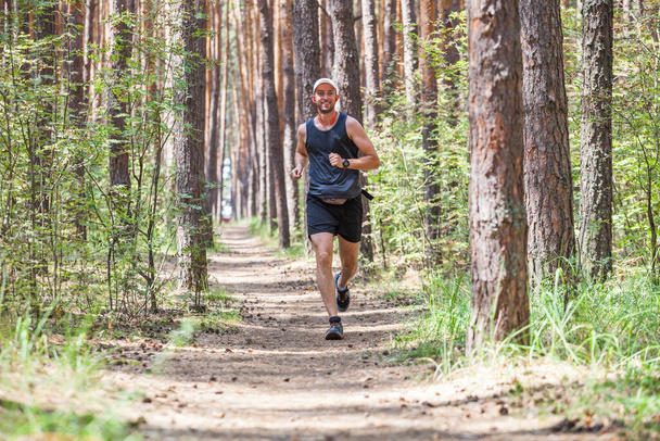 Un homme souriant en noir. Faire du jogging dans la forêt de pins  - Photo, image