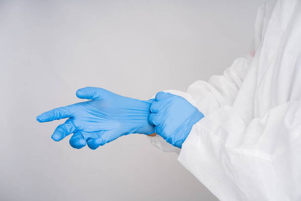医者はPPEスーツを着ていて青いゴム手袋をしている。孤立した背景。専門的なケア、診断の概念. - 写真・画像