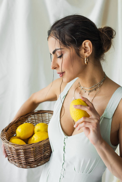 гарна жінка в сукні тримає плетений кошик і лимон на білому
 - Фото, зображення