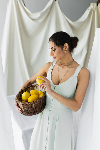 vrouw in jurk houden rijpe citroenen in rieten mand op wit - Foto, afbeelding