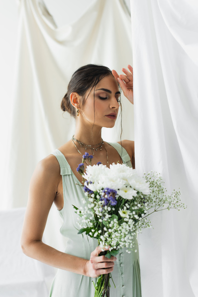 brunette woman in dress posing with bouquet of flowers on white - Foto, afbeelding