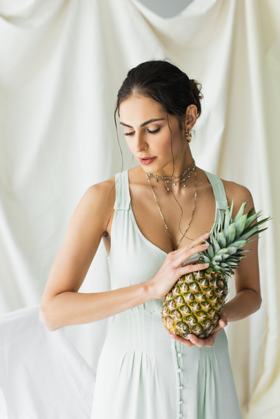 brunette woman in dress posing with pineapple on white  - 写真・画像