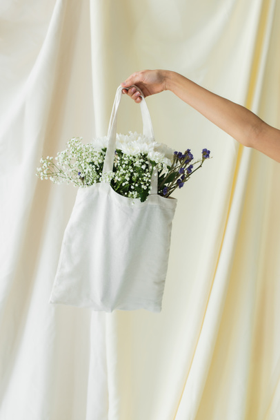 vista recortada de la mujer sosteniendo bolso de comprador de tela con flores en blanco - Foto, Imagen