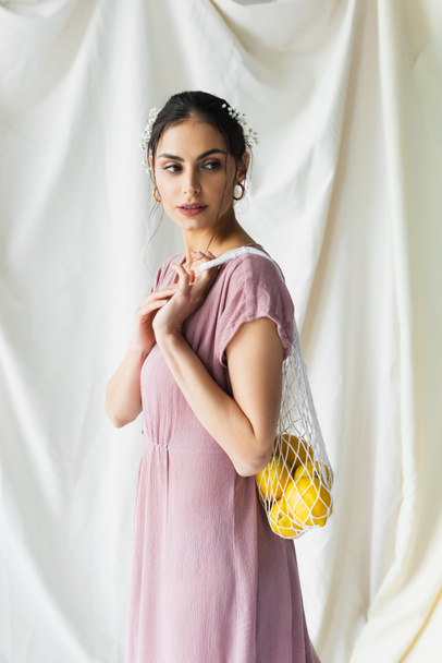 brunette woman holding reusable string bag with lemons on white - Fotoğraf, Görsel