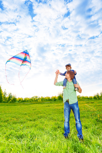 Smiling father holds kid and watches kite in air - Photo, image