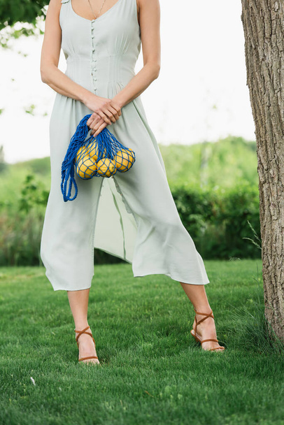 cropped view of woman holding reusable string bag with lemons in park - Photo, image