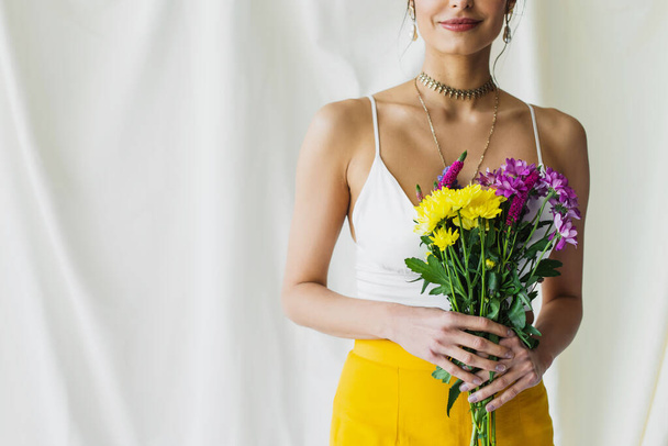 cropped view of happy woman in crop top holding flowers on white - Foto, Imagem