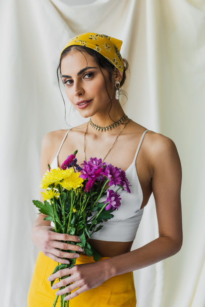 brunette woman in yellow headscarf holding flowers on white - Фото, изображение