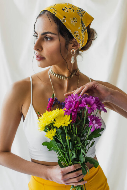 woman in yellow headscarf holding bouquet of flowers on white - Foto, afbeelding