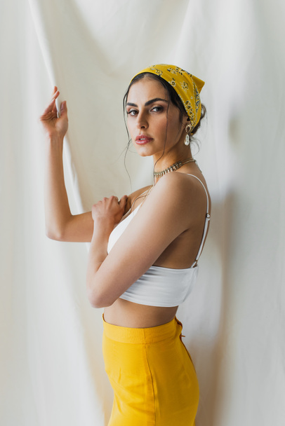 woman in yellow headscarf and crop top looking at camera on white - Фото, изображение