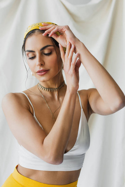 woman in yellow headscarf and crop top posing while looking away on white - Foto, Bild