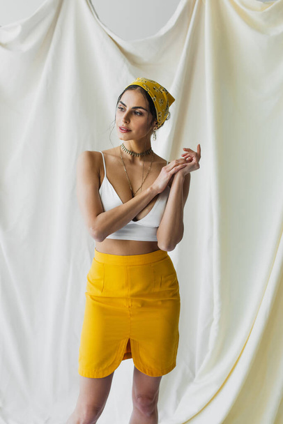 stylish woman in yellow headscarf, skirt and crop top posing on white - Foto, Bild