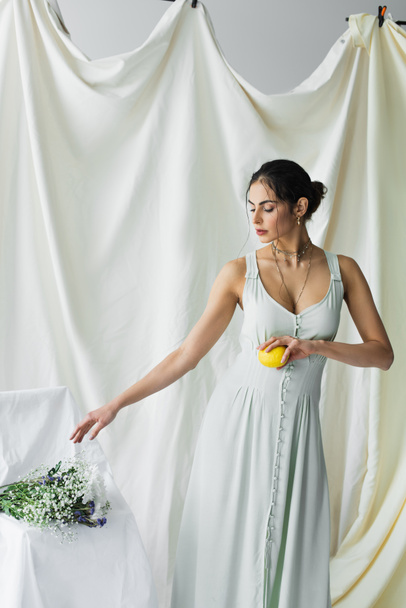 pretty woman reaching flowers while holding fresh lemon on white - Foto, imagen