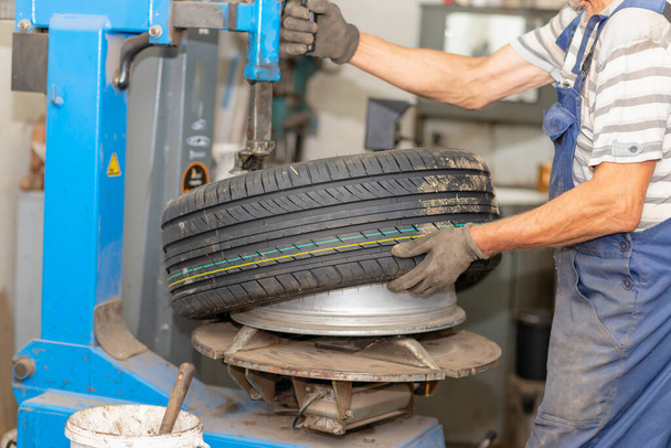 Mécanicien changer de pneu en service de voiture. Machine de rotation des pneus.Mécanicien automobile monte pneu sur roue dans un atelier. installation de pneus dans l'atelier, gros plan. - Photo, image