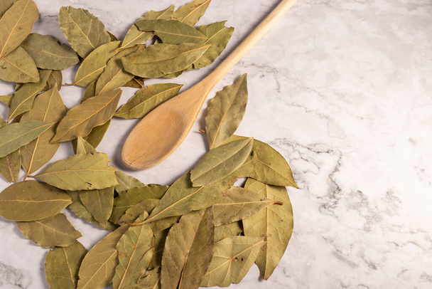 A closeup of bay leaves and a wooden spoon on the white marble surface. - Foto, immagini