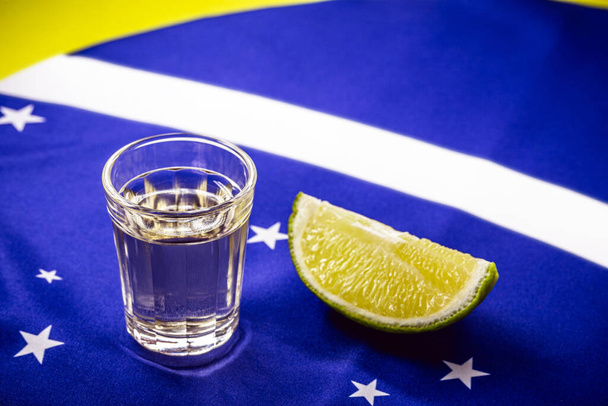 vaso de bebida destilada hecha de caña de azúcar, sobre la bandera brasileña, concepto de la pinga nacional y el día de la cachaca - Foto, imagen