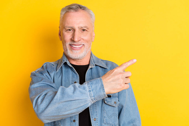 Photo of funny mature grandpa point empty space wear jeans jacket isolated on vivid yellow color background - Fotografie, Obrázek