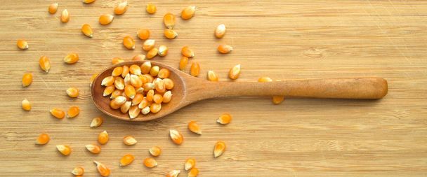 Keltainen maissi maissi jyvät valmis tekemään popcornia, leikkuulauta bambu ja puinen lusikka - Valokuva, kuva