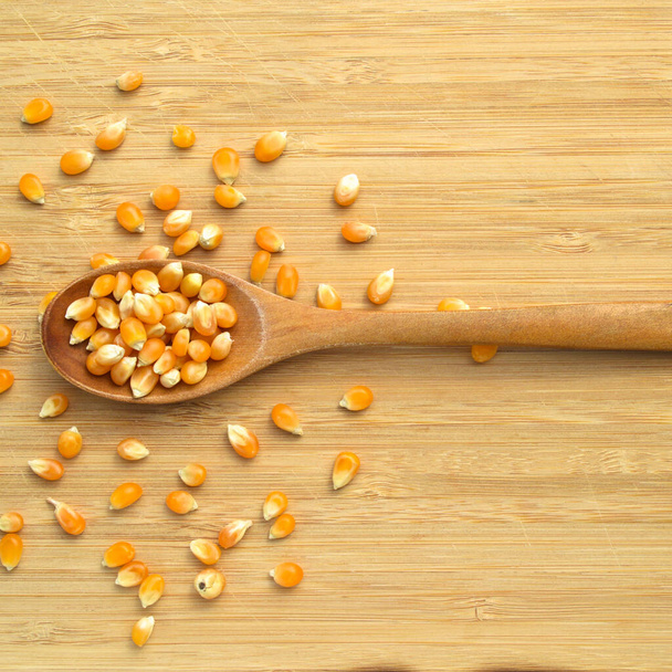 Chicchi di mais giallo pronti per la preparazione di popcorn, su tagliere di bambù e in cucchiaio di legno - Foto, immagini