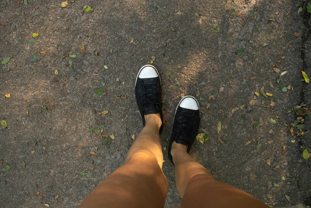 Kadın bacakları siyah beyaz spor ayakkabılarla parkta güneş altında, bacakları asfaltta. - Fotoğraf, Görsel